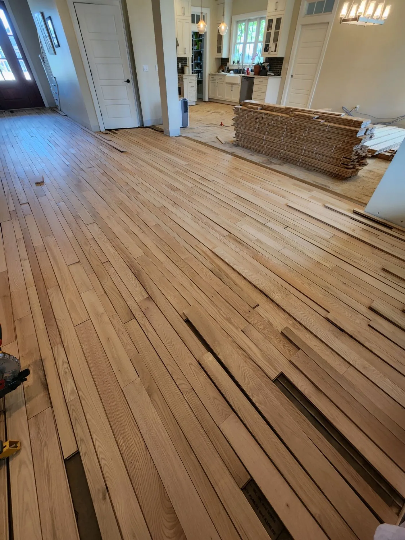 Hardwood plank installation in a kitchen with stacked oak boards ready to lay