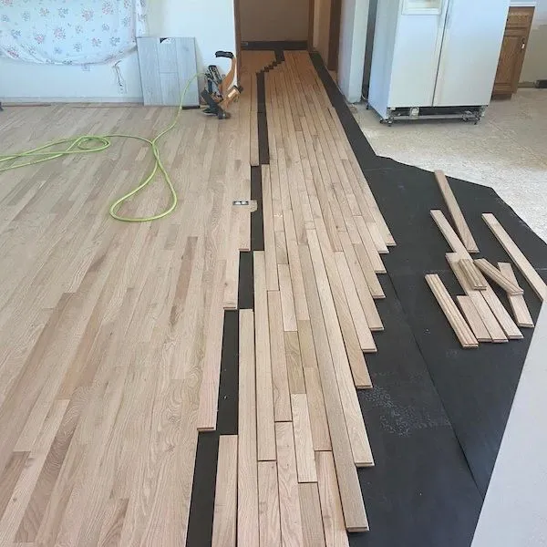 Hardwood floor installation showing staggered plank layout on black underlayment