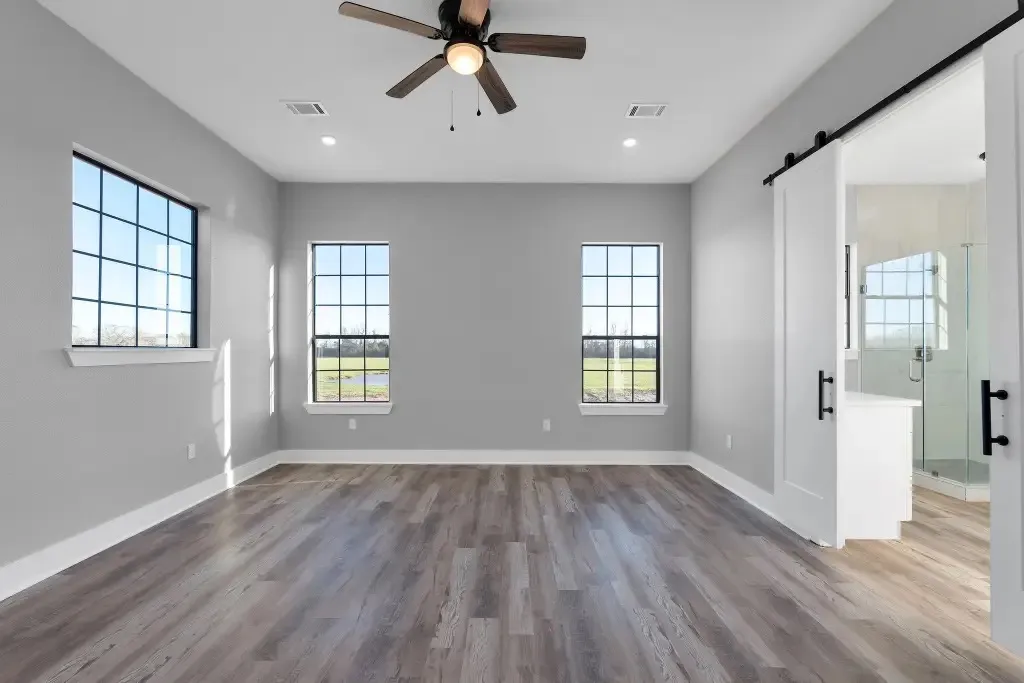 Luxury vinyl plank flooring in a modern bedroom with barn door and ceiling fan