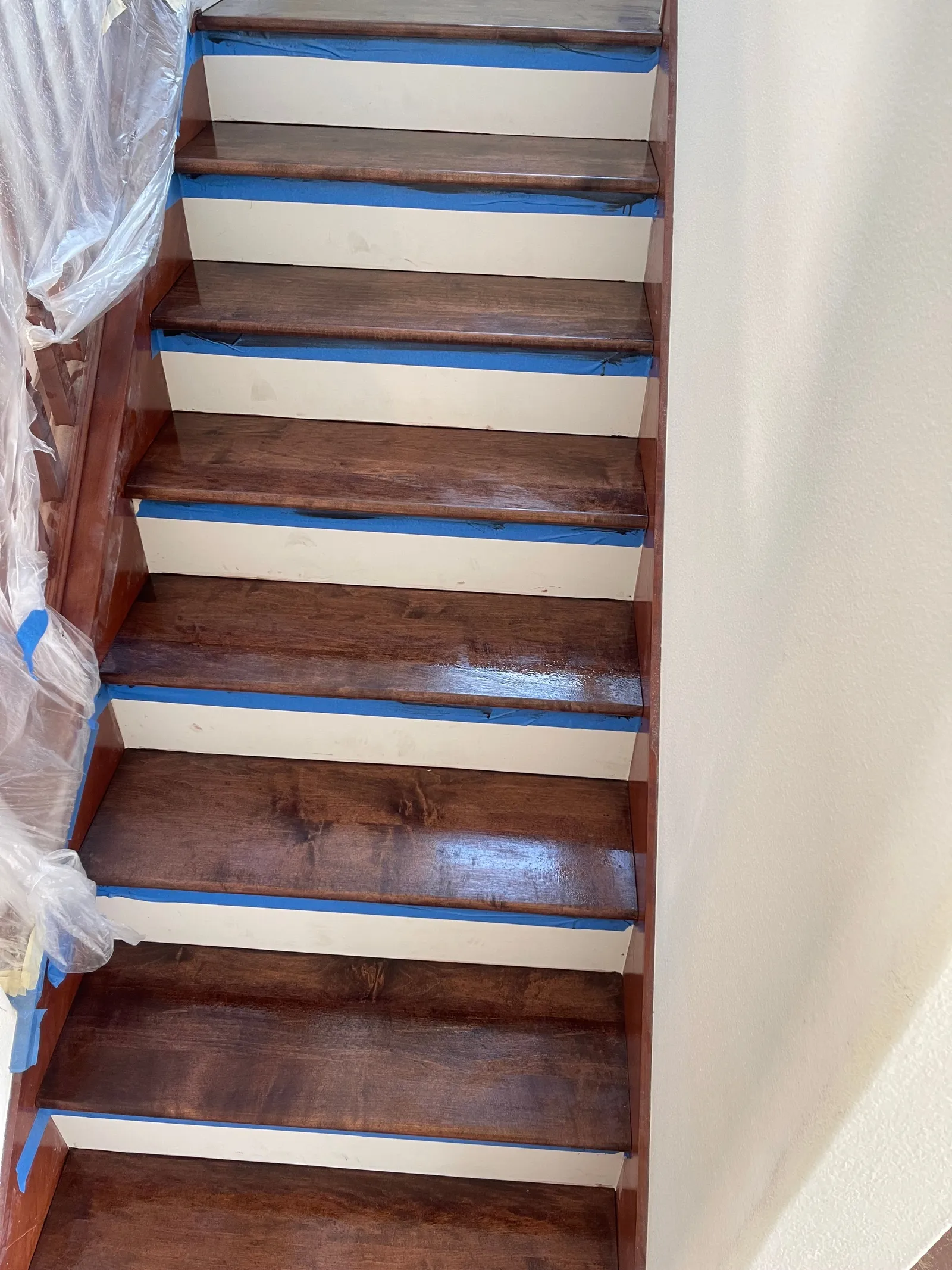 Stair refinishing in progress with dark walnut stain and blue painter tape on risers